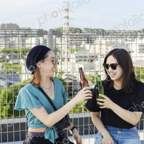 Two young Japanese women sitting on a rooftop in an urban setting, drinking beer. Two young Japanese women sitting on a rooftop in an urban setting, drinking beer.