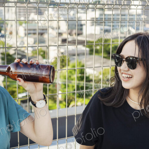 Two young Japanese women sitting on a rooftop in an urban setting, drinking beer. Two young Japanese women sitting on a rooftop in an urban setting, drinking beer.