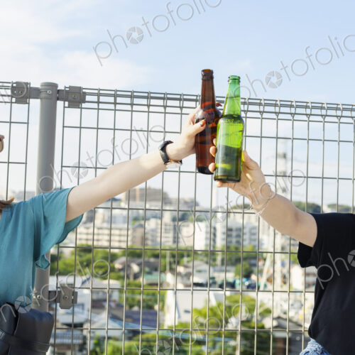 Two young Japanese women sitting on a rooftop in an urban setting, drinking beer. Two young Japanese women sitting on a rooftop in an urban setting, drinking beer.