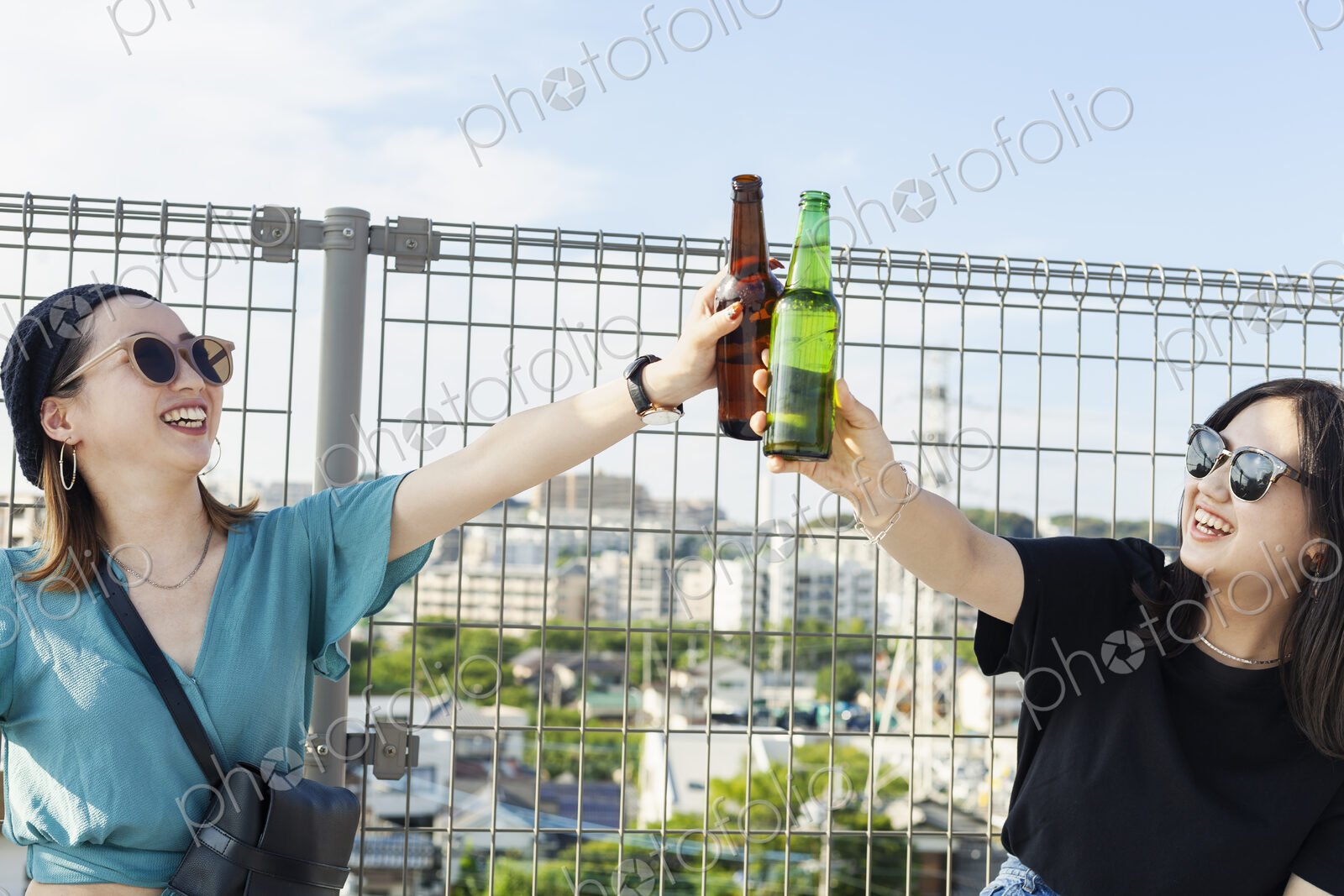 Two young Japanese women sitting on a rooftop in an urban setting, drinking beer.