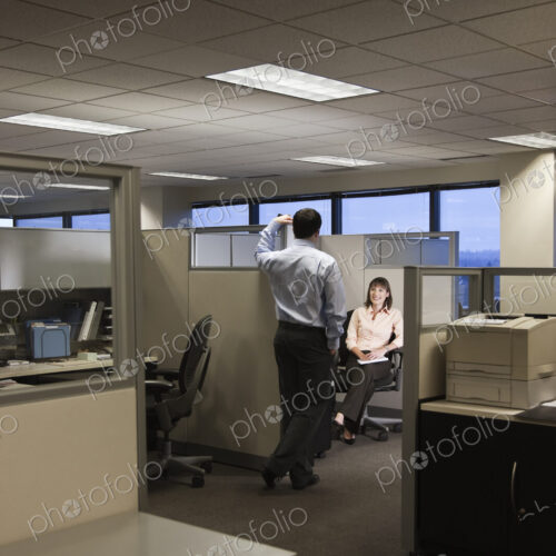 Two young business people working into the evening in a cubicle office set up. Two young business people working into the evening in a cubicle office set up.