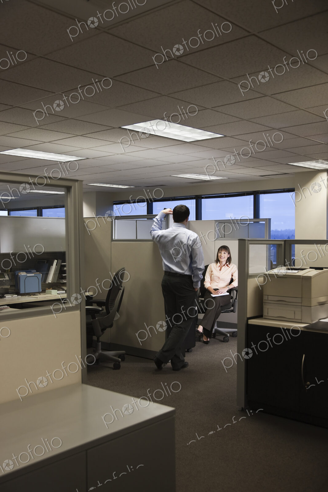 Two young business people working into the evening in a cubicle office set up.