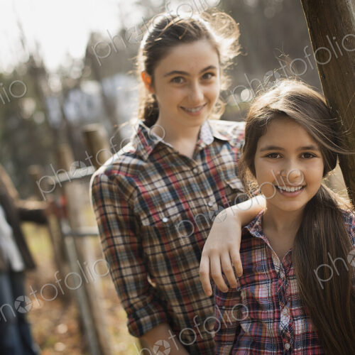 Two young girls beside a paddock fence, and a man in the background. An organic farm. Two young girls beside a paddock fence, and a man in the background. An organic farm.