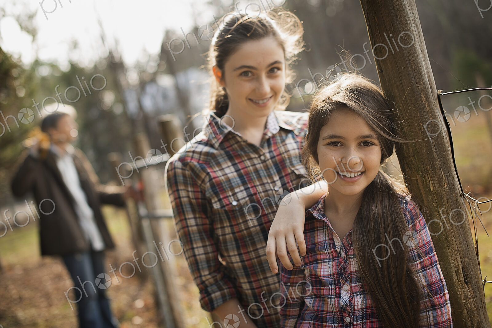 Two young girls beside a paddock fence, and a man in the background. An organic farm.