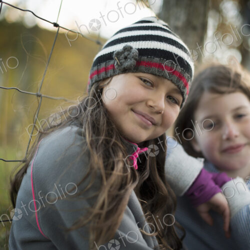 Two young girls side by side outdoors on a farm. Leaning on a fence post. Two young girls side by side outdoors on a farm. Leaning on a fence post.