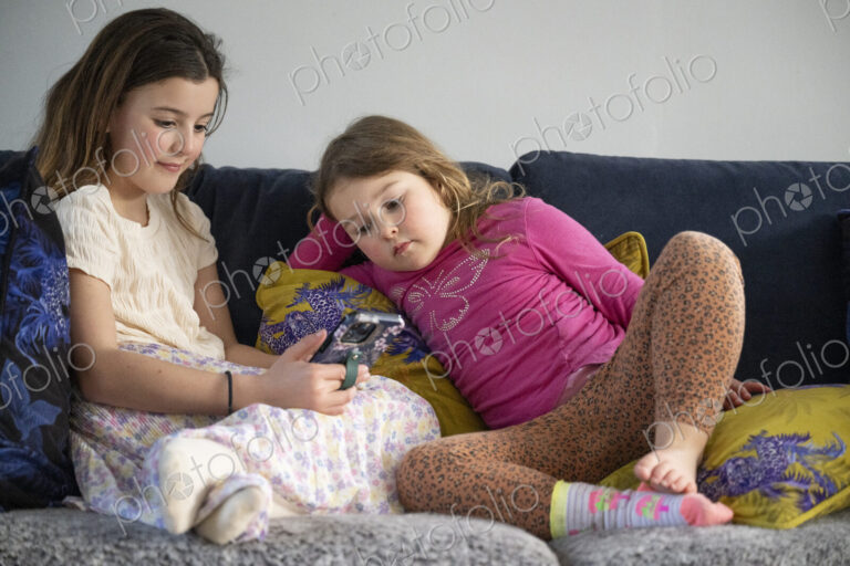 Two young girls sitting on sofa looking at smart phone.