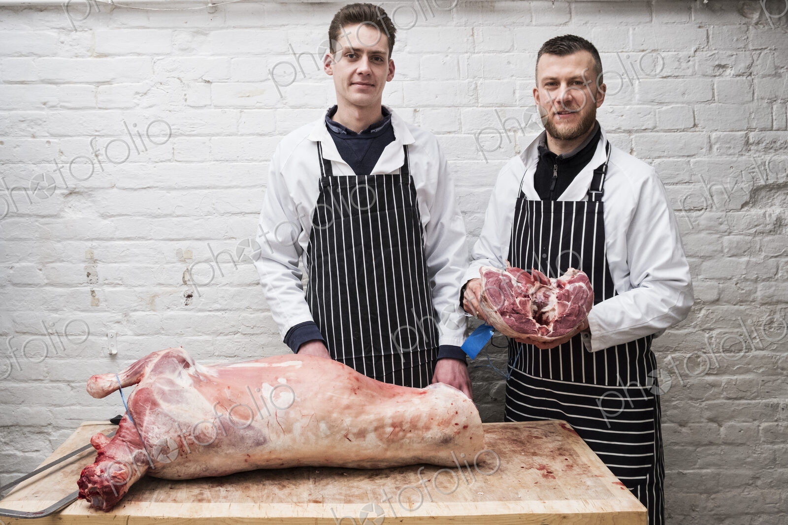 Two young men working, butchers jointing a whole lamb carcass.