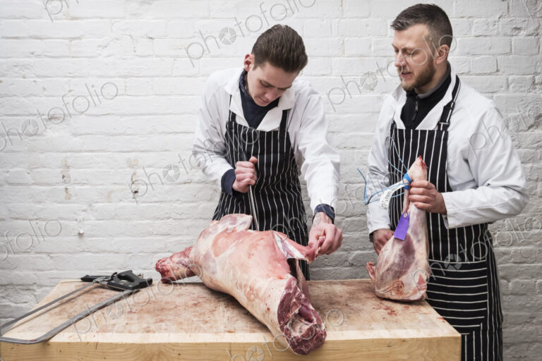 Two young men working, butchers jointing a whole lamb carcass.