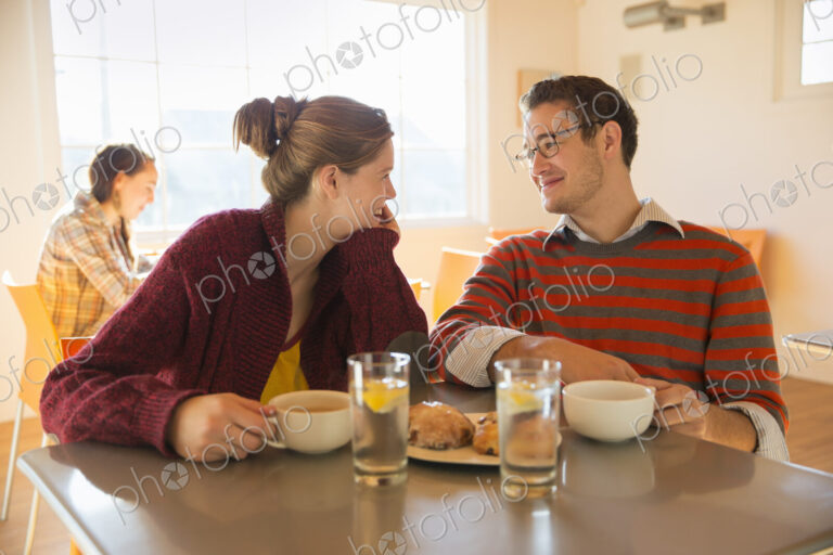 Two young people, a man and a young woman sitting at a counter in a coffee shop.