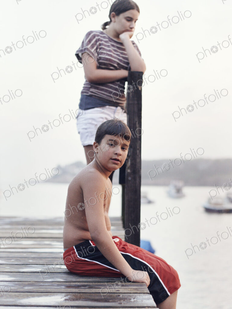 Two young people, teenagers, boy and girl, on a dock overlooking moored boats on the…
