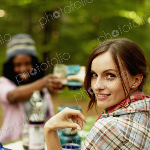 Two young woman drinking a toast at a picnic site or campsite in the woods.