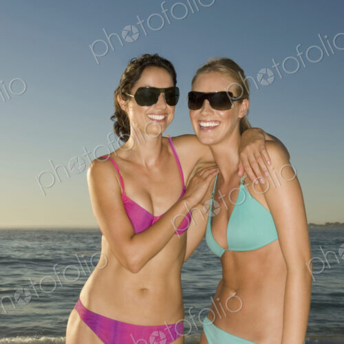 Two young women on the beach in Cape Town, wearing bikinis and sunglasses.