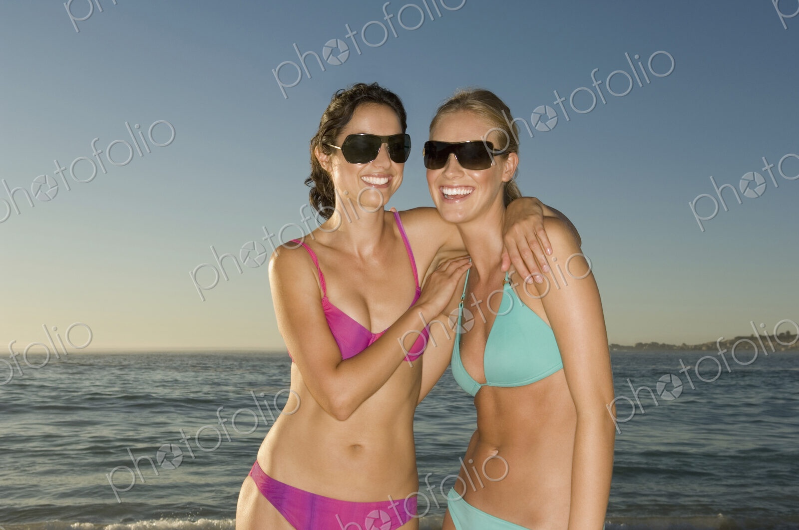 Two young women on the beach in Cape Town, wearing bikinis and sunglasses.