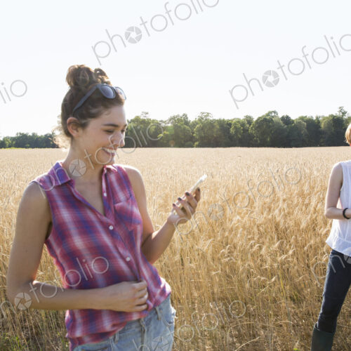 Two young women standing in a cornfield, one holding her mobile phone. Two young women standing in a cornfield, one holding her mobile phone.