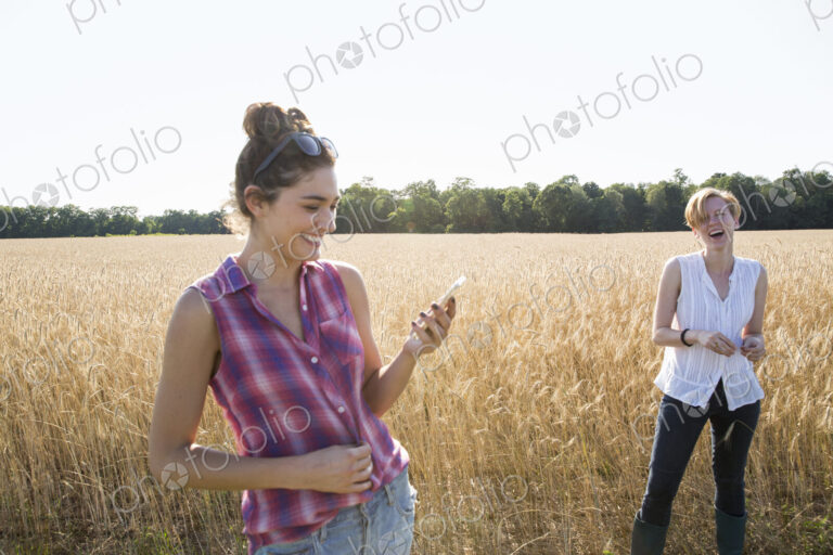 Two young women standing in a cornfield, one holding her mobile phone.