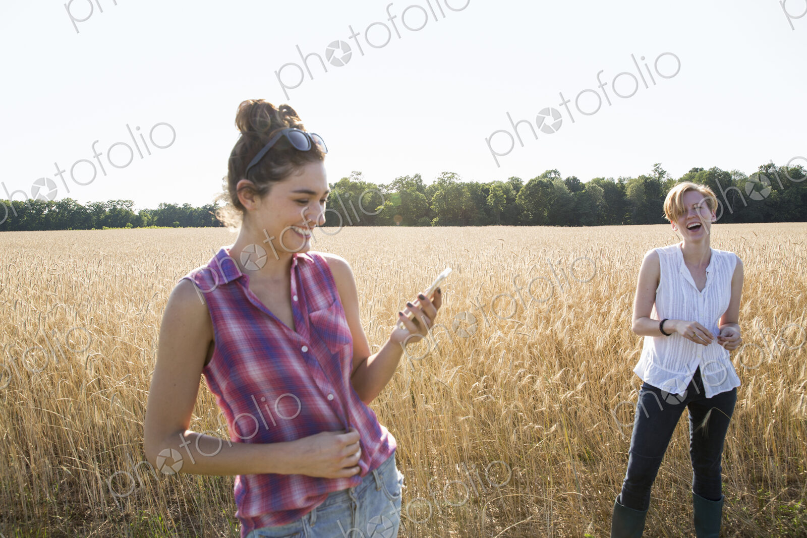 Two young women standing in a cornfield, one holding her mobile phone.
