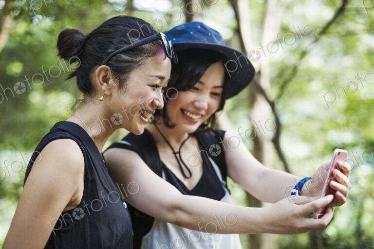 Two young women standing in a forest, taking a selfie.