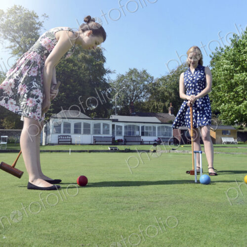 Two young women standing on a lawn, playing croquet. Two young women standing on a lawn, playing croquet.