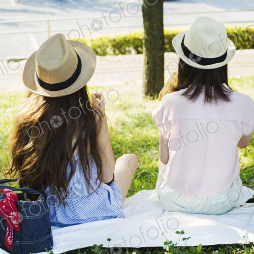 Two young women with long brown hair sitting on a lawn.