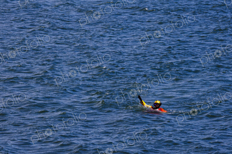 US Coast Guard helicopter demo rescue with rescue swimmer in the water with a raised hand.