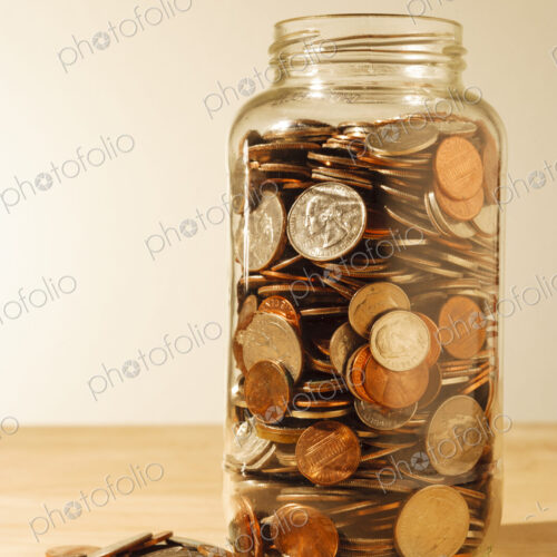 US coins collected in a glass jar, quarters, dollars, nickels and dimes.