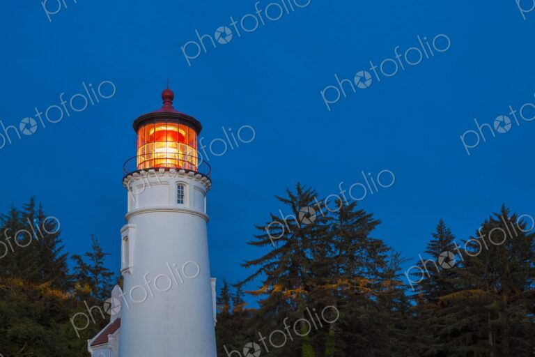 Umpqua Lighthouse illuminated at dusk, standing tall among coastal trees in Winchester…