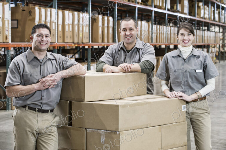 Uniformed warehouse workers surrounded by boxed products in a large distribution…