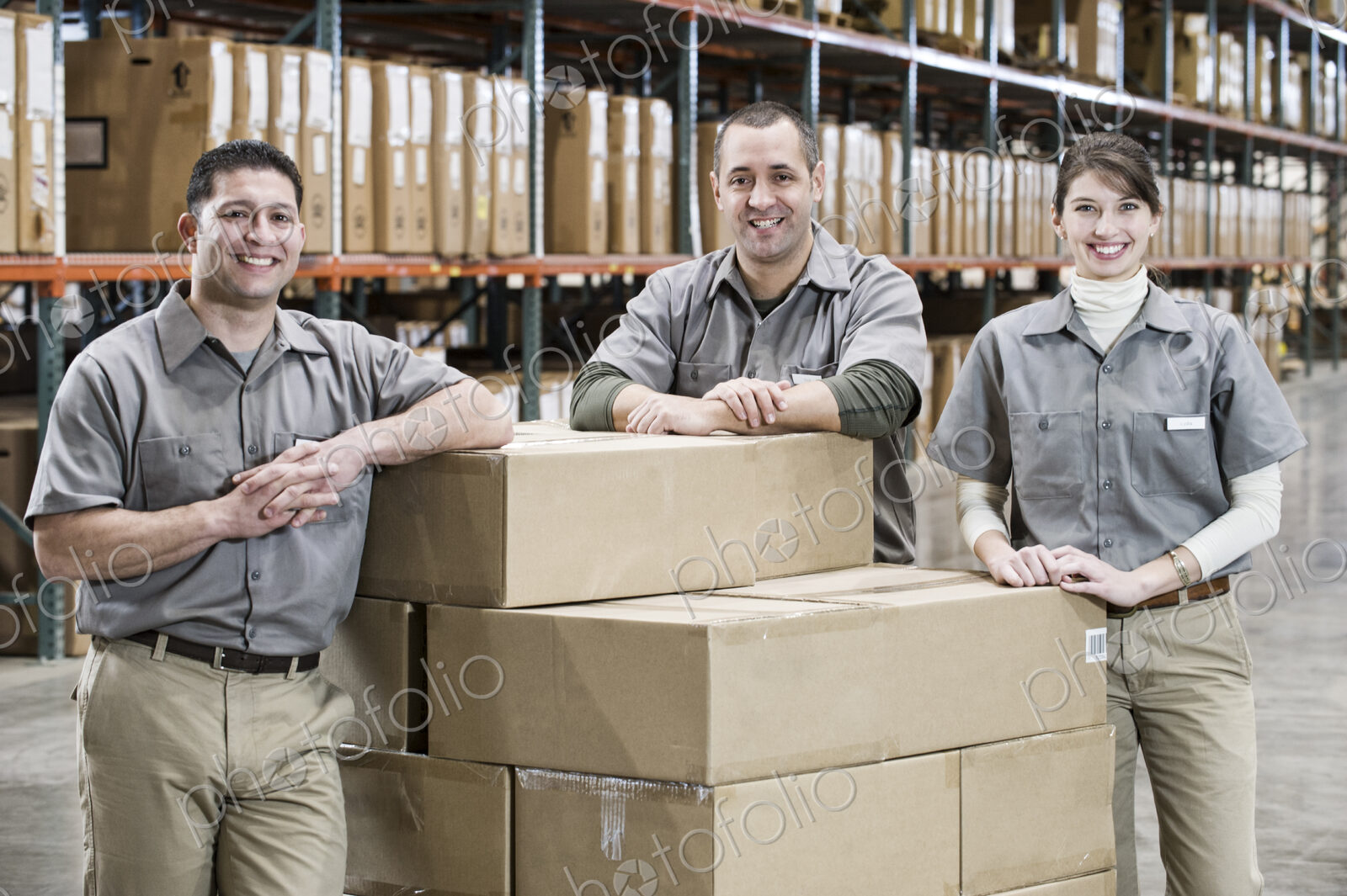 Uniformed warehouse workers surrounded by boxed products in a large distribution…