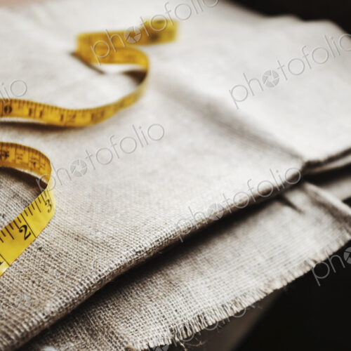 Upholstery workshop. Neutral coloured folded furnishing fabric and a yellow tape measure. Upholstery workshop. Neutral coloured folded furnishing fabric and a yellow tape measure.