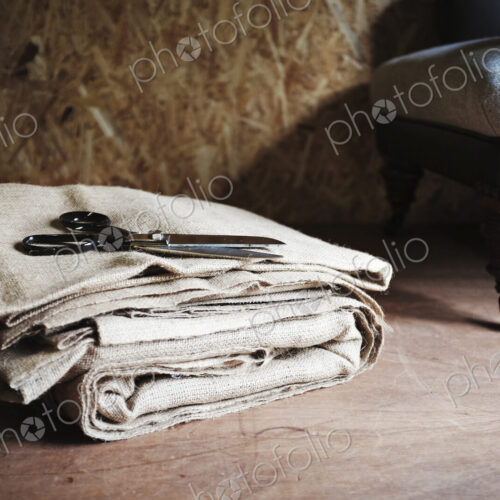 Upholstery workshop. Neutral coloured folded furnishing fabric, large scissors and a…
