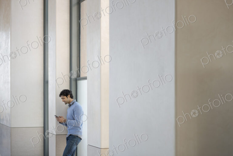 Urban Lifestyle. A man in a blue sweater using his mobile phone. An empty building.