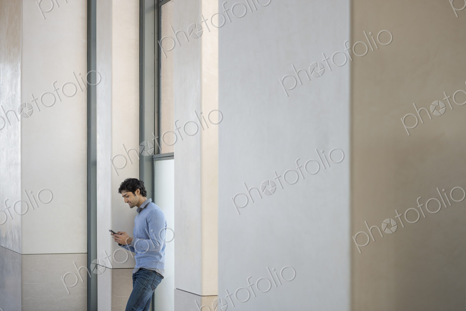 Urban Lifestyle. A man in a blue sweater using his mobile phone. An empty building.