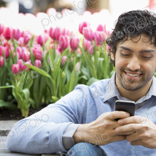 Urban Lifestyle. A man in the park, using his mobile phone. A bed of pink flowering… Urban Lifestyle. A man in the park, using his mobile phone. A bed of pink flowering…