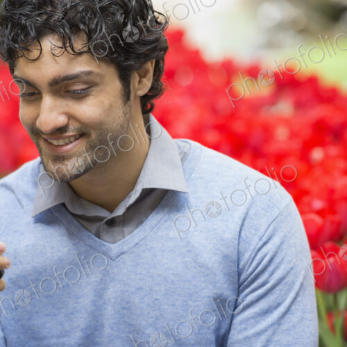 Urban Lifestyle. A man in the park, using his mobile phone. A bed of red flowering… Urban Lifestyle. A man in the park, using his mobile phone. A bed of red flowering…