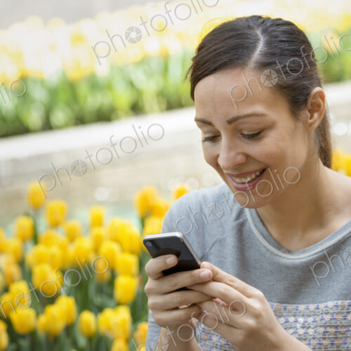 Urban Lifestyle. A woman in the park, by a bed of yellow tulips, using her mobile phone. Urban Lifestyle. A woman in the park, by a bed of yellow tulips, using her mobile phone.