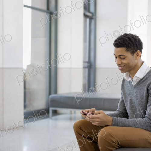 Urban Lifestyle. A young man sitting in a lobby, on a bench seat. Using his mobile phone. Urban Lifestyle. A young man sitting in a lobby, on a bench seat. Using his mobile phone.