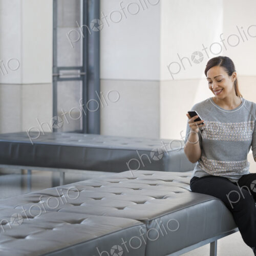 Urban Lifestyle. A young woman sitting on a seat in a building, using her mobile phone. Urban Lifestyle. A young woman sitting on a seat in a building, using her mobile phone.