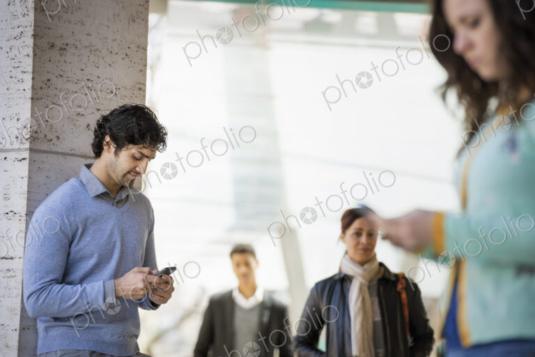 Urban Lifestyle. Three people on the sidewalk, a man and a young woman using their…