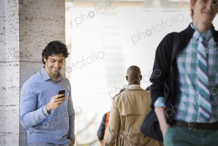 Urban Lifestyle. Three people on the sidewalk, a man using his mobile phone, a man in…