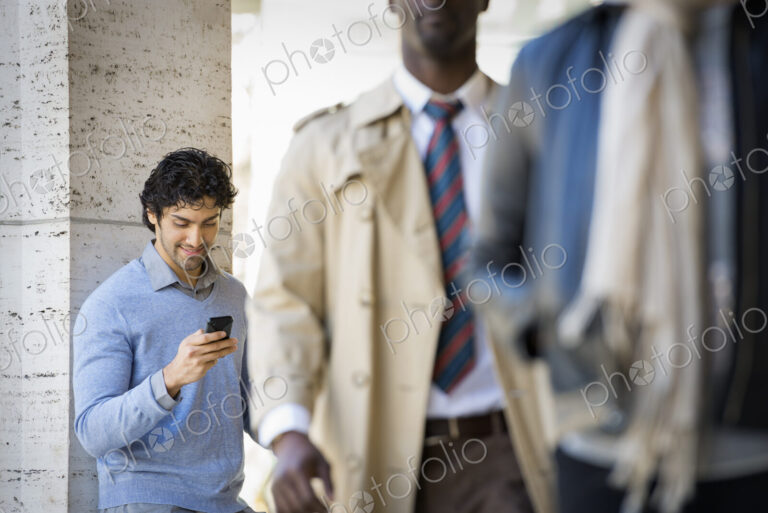 Urban Lifestyle. Three people on the sidewalk, a man using his mobile phone, a man in…