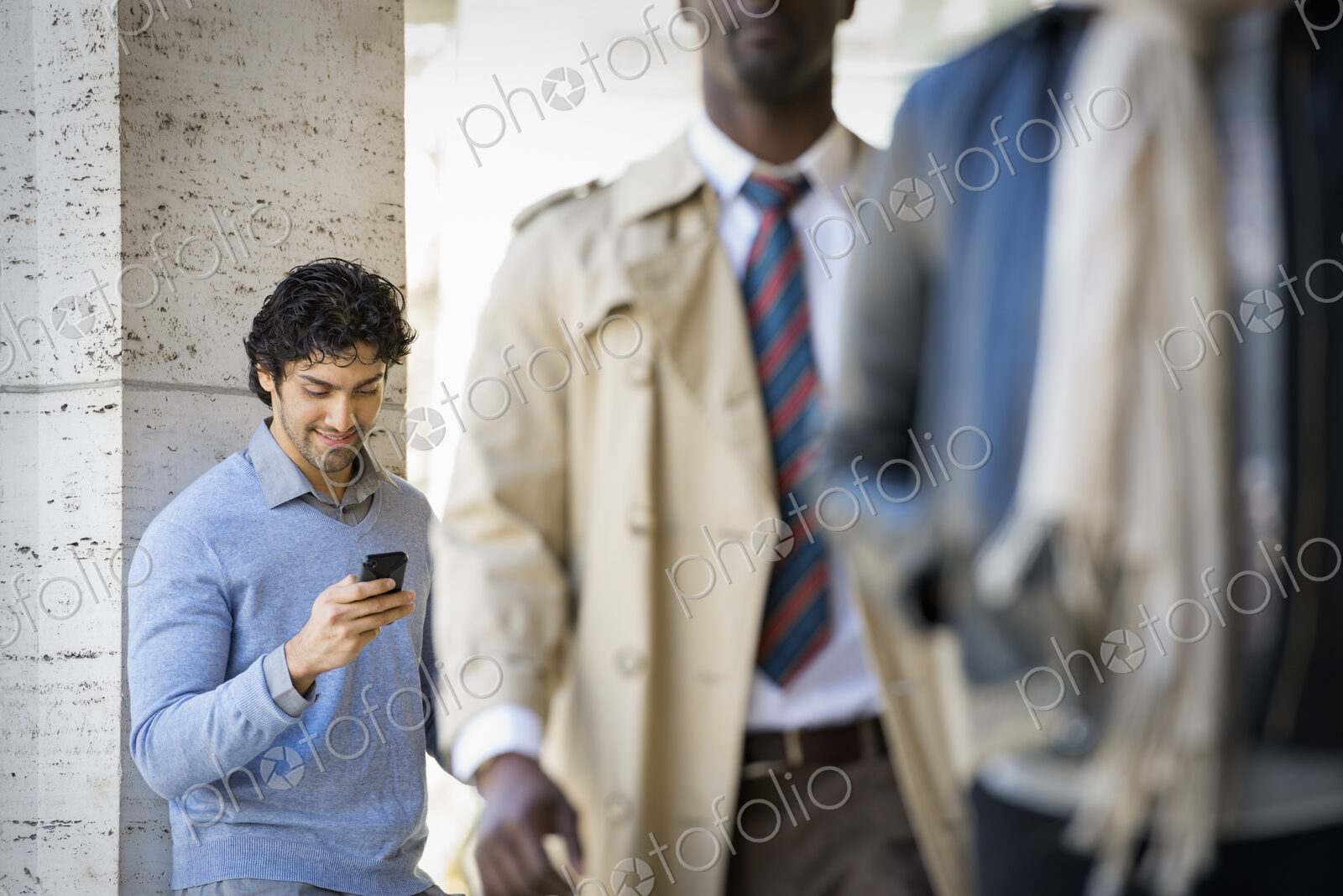 Urban Lifestyle. Three people on the sidewalk, a man using his mobile phone, a man in…