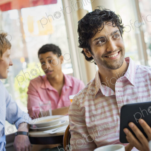 Urban Lifestyle. Three young men around a table in a cafe. One holding a digital tablet. Urban Lifestyle. Three young men around a table in a cafe. One holding a digital tablet.