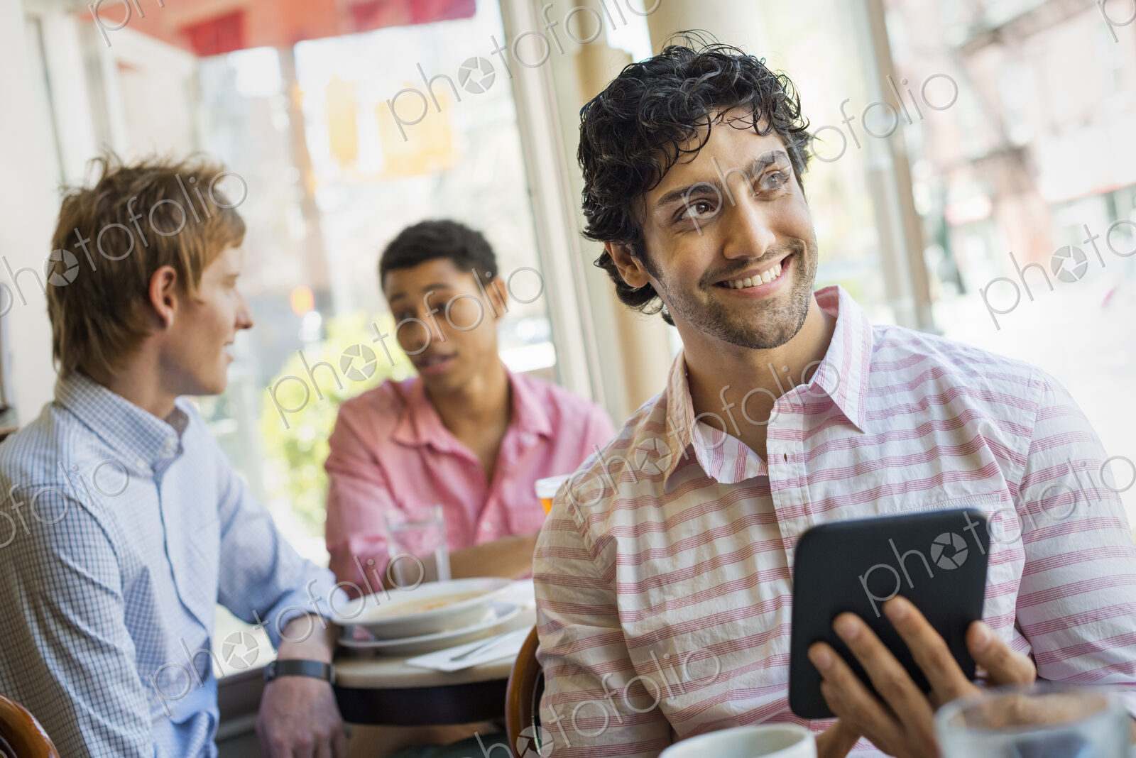 Urban Lifestyle. Three young men around a table in a cafe. One holding a digital tablet.