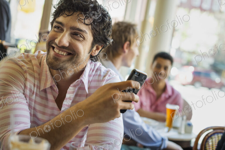 Urban Lifestyle. Three young men around a table in a cafe. One using his smart phone