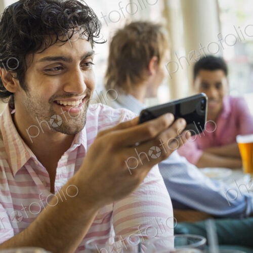 Urban Lifestyle. Three young men around a table in a cafe. One using his smart phone Urban Lifestyle. Three young men around a table in a cafe. One using his smart phone