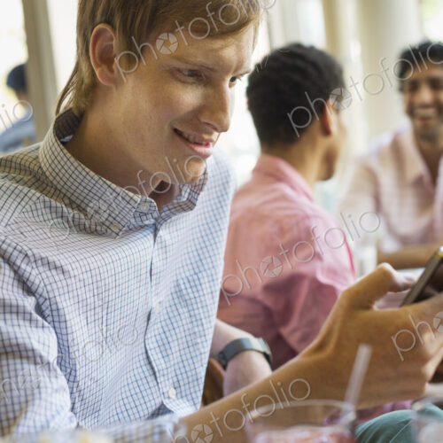 Urban Lifestyle. Three young men in a cafe. One checking his smart phone. Two talking… Urban Lifestyle. Three young men in a cafe. One checking his smart phone. Two talking…