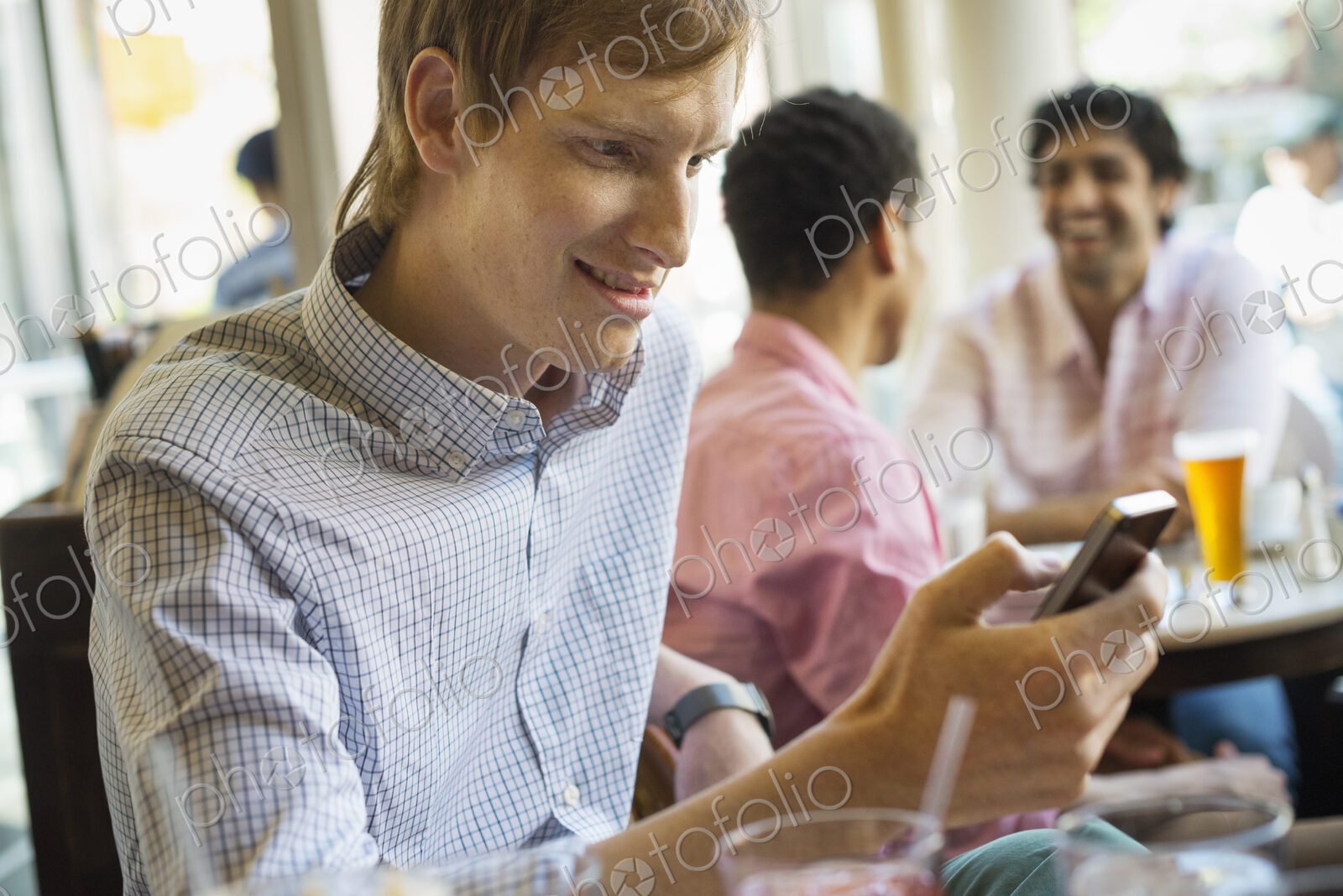 Urban Lifestyle. Three young men in a cafe. One checking his smart phone. Two talking…