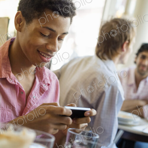 Urban Lifestyle. Three young men in a cafe. One checking his smart phone. Two talking… Urban Lifestyle. Three young men in a cafe. One checking his smart phone. Two talking…
