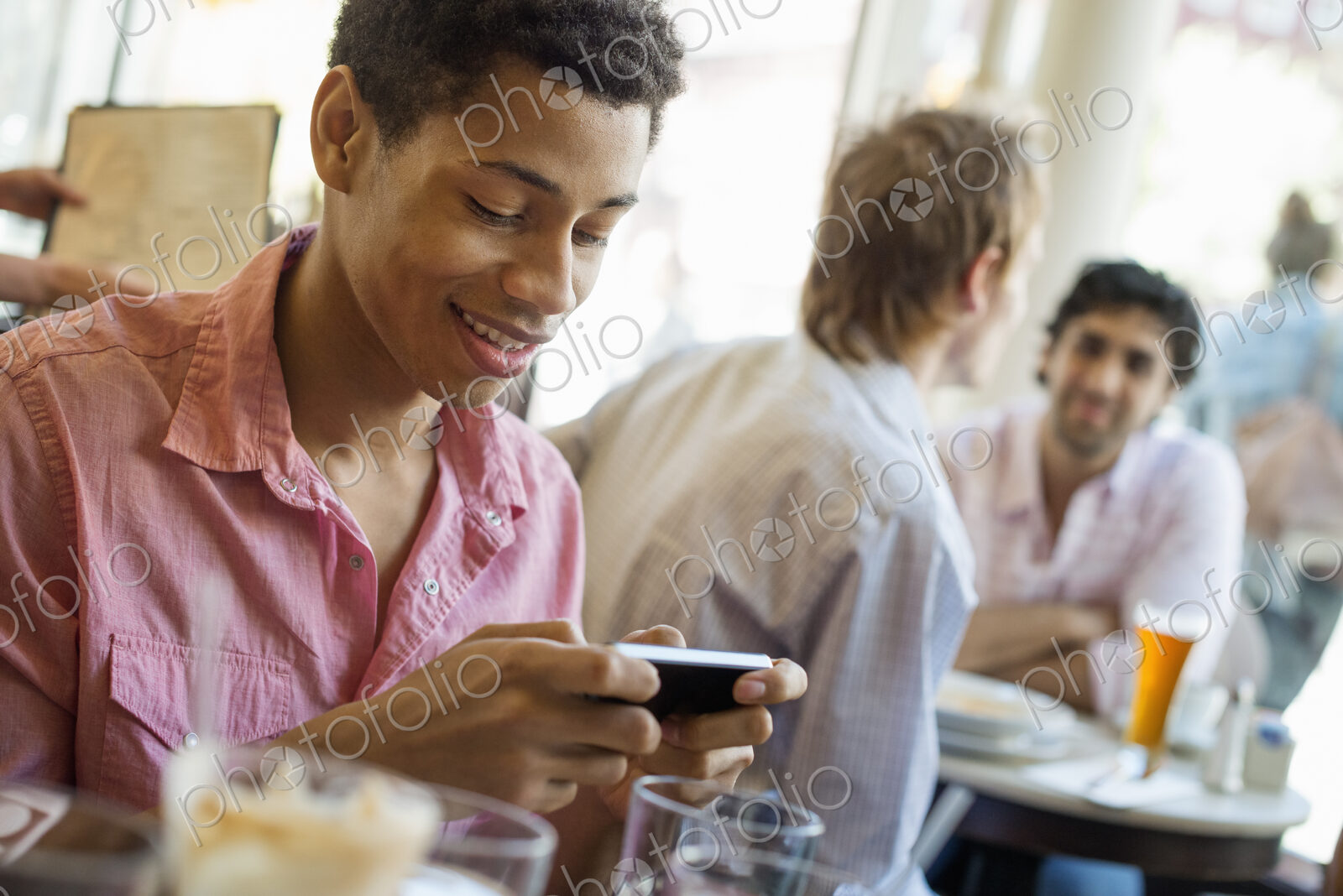Urban Lifestyle. Three young men in a cafe. One checking his smart phone. Two talking…