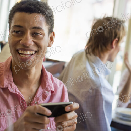 Urban Lifestyle. Three young men in a cafe. One checking his smart phone. Two talking… Urban Lifestyle. Three young men in a cafe. One checking his smart phone. Two talking…